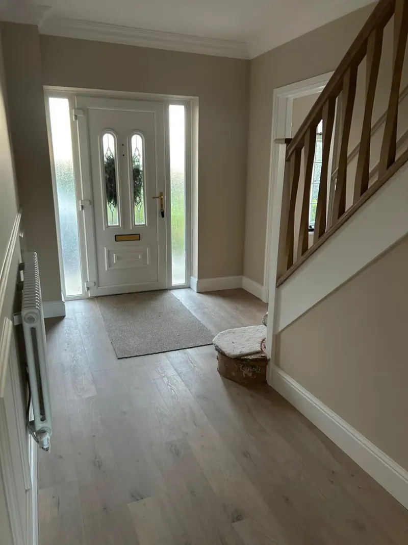 Completed entrance hallway renovation with white door and oak flooring